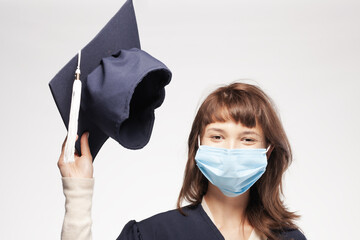 Graduation girl with gown throwing cap smiling. Happy female student wearing protective face mask.