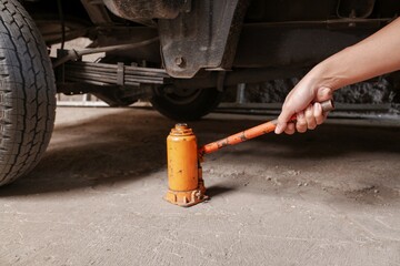 Hand holding orange hydraulic bottle lever is installed under car, stock photo.