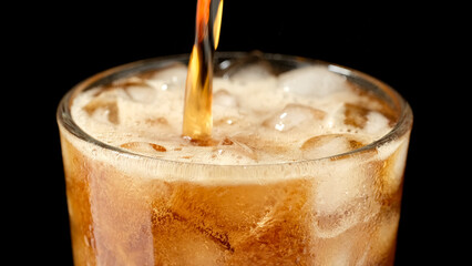 pouring refreshing drink into glass with ice, black background
