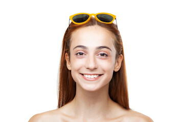 Portrait of a cheerful young woman with long red hair and sunglasses perched atop her head, smiling brightly on a white background.
