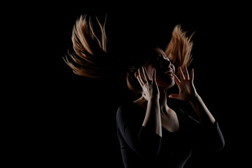 A striking image of a woman captured with her hair dramatically tossed in the air, silhouetted against a pure black background, emphasizing movement and emotion.