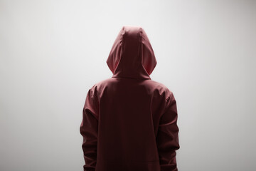 Mysterious young woman in maroon hoodie facing away on plain background