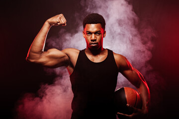 Basketball player side lit with red color holding a ball against hazy smoke fog background. Serious...