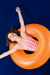 Happy girl in one piece pink swimsuit enjoyng and lying on inflatable orange rubber ring. Summer...