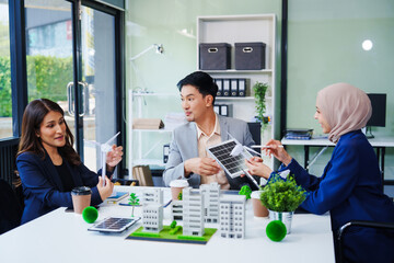 Trio of businesspeople, including a middle-aged Asian man and woman, strategize at their desk,...