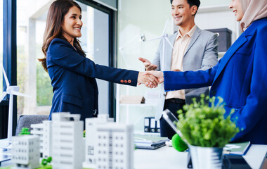 Three businesspeople convene at a desk with handshakes. middle-aged Asian man and woman discuss...