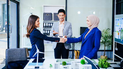 Three businesspeople convene at a desk with handshakes. middle-aged Asian man and woman discuss...