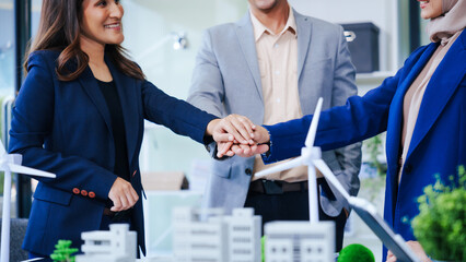 Three businesspeople gather at a desk, symbolizing unity with joined hands. Led by a middle-aged...