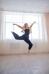 Caucasian woman dances contemporary in ballet class. Dancer in a jump. Vertical photo.