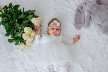 festively dressed baby girl lies on white with flowers. celebration