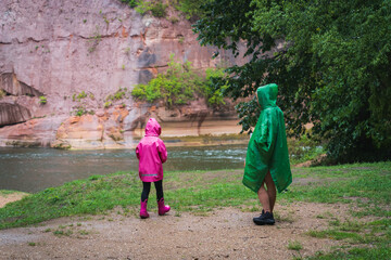 Mom and daughter in raincoats outdoors on a rainy summer day.