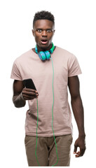 Young african american man wearing headphones and holding smartphone scared in shock with a surprise face, afraid and excited with fear expression