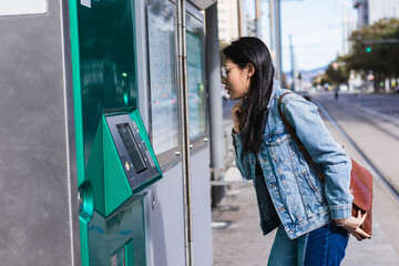 Young woman buying train ticket at automatic vending machine