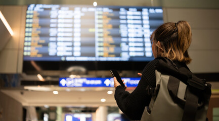 Young Asian woman in international airport looking at flight information board, checking her flight