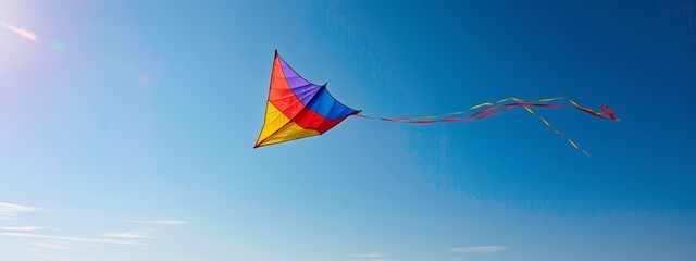 A clear sky with a single, colorful kite soaring high with a long tail.