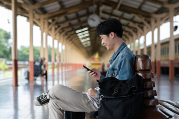 Young man with backpack checking social media on phone waiting for train at train station to travel