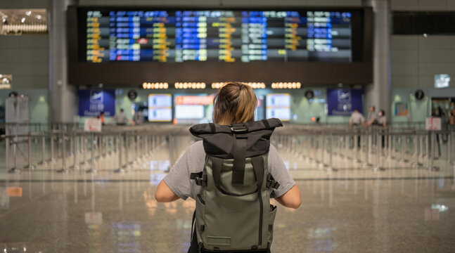 Young Asian woman in international airport looking at flight information board, checking her flight