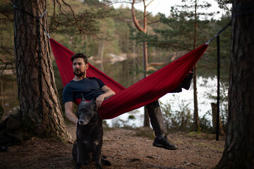 Man and dog chilling in a hammock after a long day in the forest with a lake in the background