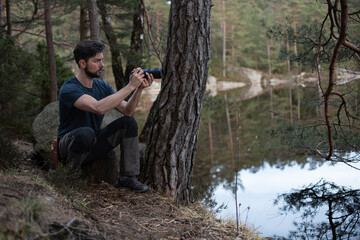 Young man photographer trying to capture an image in the forest in summer by a lake