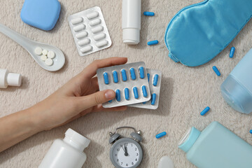 Sleep mask, plastic bottles and jars, alarm clock and pills in hand on light background, top view