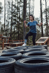 Young asian woman doing exercise in outdoor gym in the forest, jumping between tires