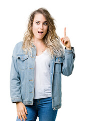 Beautiful young blonde woman wearing denim jacket over isolated background pointing finger up with successful idea. Exited and happy. Number one.