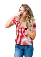 Beautiful young blonde woman over isolated background smelling something stinky and disgusting, intolerable smell, holding breath with fingers on nose. Bad smells concept.