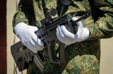 Soldier in camouflage clothes and white gloves with weapon in hands. Light background.