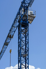 Construction crane against the sky. Tall blue tower crane. Construction site. Industrial crane equipment at a construction site. Technology for transporting materials to heights. Housing construction.