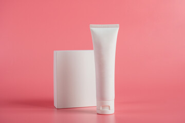 Plastic white tube for cream or lotion. Skin care or sunscreen cosmetic with stylish props on pink...