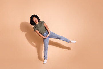 Full size photo of cheerful person wear khaki t-shirt denim trousers dancing standing on one foot isolated on pastel color background