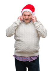 Handsome senior man wearing christmas hat over isolated background covering ears with fingers with annoyed expression for the noise of loud music. Deaf concept.