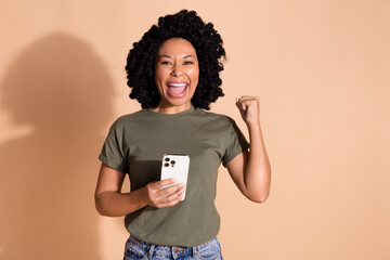 Portrait of ecstatic person wear khaki t-shirt hold smartphone clecnhing fist scream yes win bet...