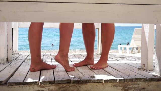 Two woman in the changing, dressing room on beach, at sunset on the seashore. Close-up of bare female feet legs in enclosed changing room cabin. Summer holiday vacation and travel concept. Slow motion