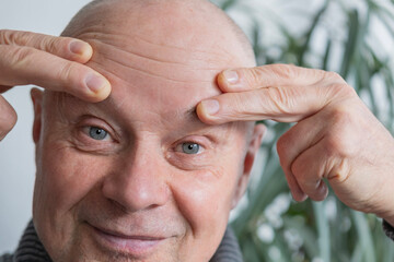 65-year-old man, senior looks carefully examines wrinkles on face, skin folds, age-related skin...