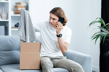 Young Man Disappointed With Online Shopping Delivery, Receiving Wrong Item While Talking On Phone, Modern Living Room Background