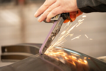 Close-up of worker using angle grinder on metal without protecting gloves, creating sparks in...