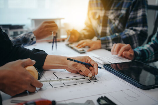 Team of engineers in a meeting, drawing blueprints for condo, apartment, and house construction. Negotiating costs with contractors, bidding, bargaining, and cooperating on construction sites.