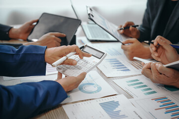 A professional business team meeting in formal suits, working at desks with financial papers, calculators, and laptops. Close-up of hands. Discussion on revenue, brand, sales, agenda, capital