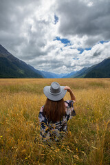 Open plains and wild grasses looking accross to Milford Sound, model wears a grey cowboy hat looking away from camera into distance