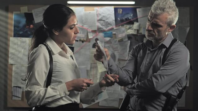 police detectives standing in office working on criminal case,couple of investigators examine files evidences discuss about crime investigation