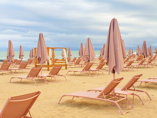 Empty beach with beige umbrellas and sun loungers before rain in summer. Beige and azure colors.
