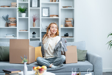 Young Woman Enjoying Phone Call While Unpacking In Modern Living Room, Surrounded By Boxes And Home...