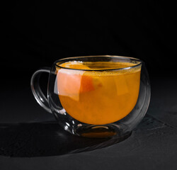 Glass mug of warm citrus tea on dark background