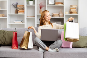 Young Woman Enjoying Online Shopping Success On Laptop, Surrounded By Colorful Shopping Bags In...