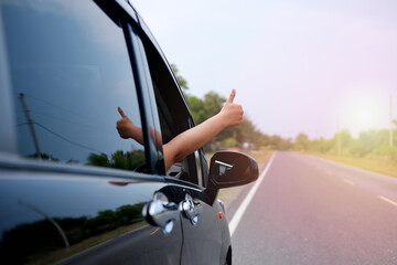 Woman inside car on the road trip with thumb up gesture out of the window with copy space for...