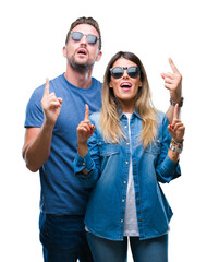 Young couple in love wearing sunglasses over isolated background amazed and surprised looking up and pointing with fingers and raised arms.