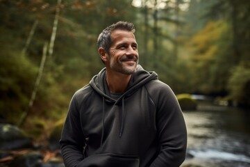 Portrait of a satisfied man in his 40s dressed in a comfy fleece pullover isolated on tranquil forest stream