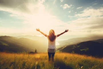 A woman stands in a field of grass, arms outstretched, with the sun shining on her. Concept of freedom and joy, as the woman is embracing the beauty of nature and the warmth of the sun