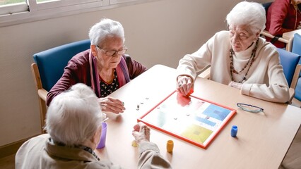 Senior woman playing ludo with friends at table in nursing home